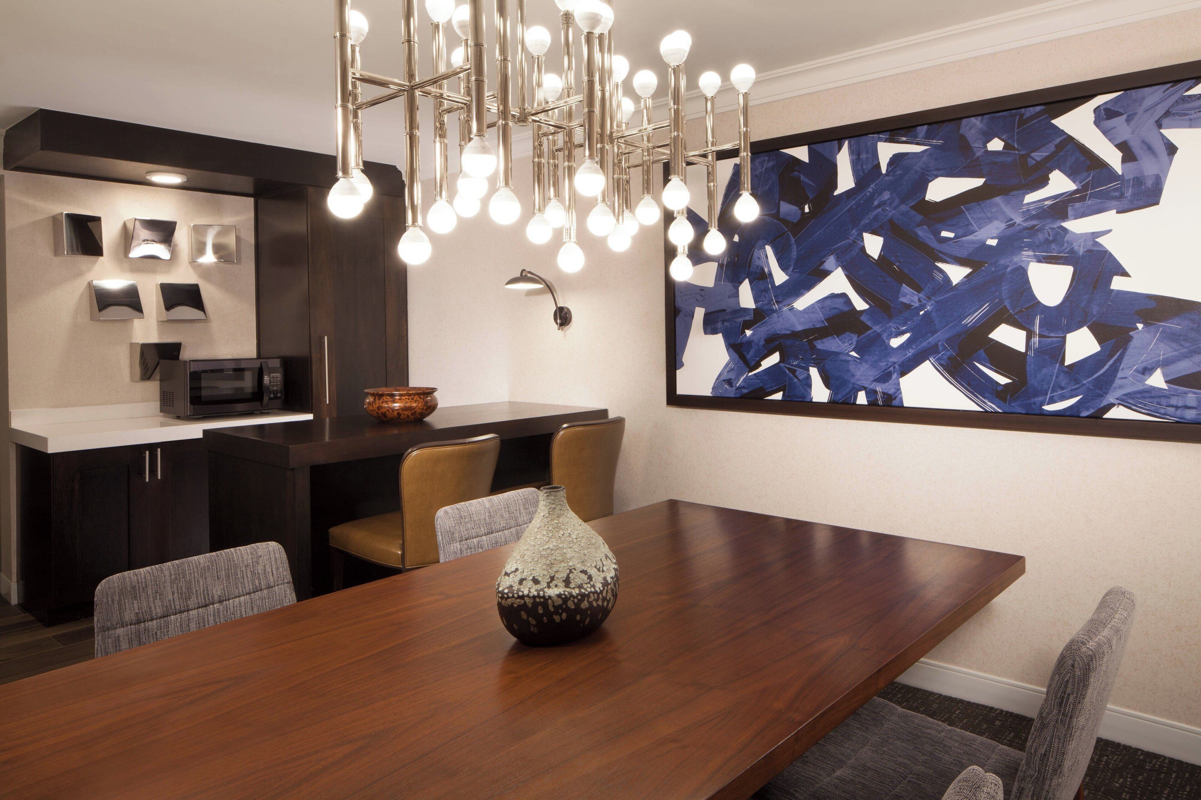 A modern dining area with a wooden table, chairs, a decorative vase, a contemporary light fixture, and a large abstract painting on the wall.