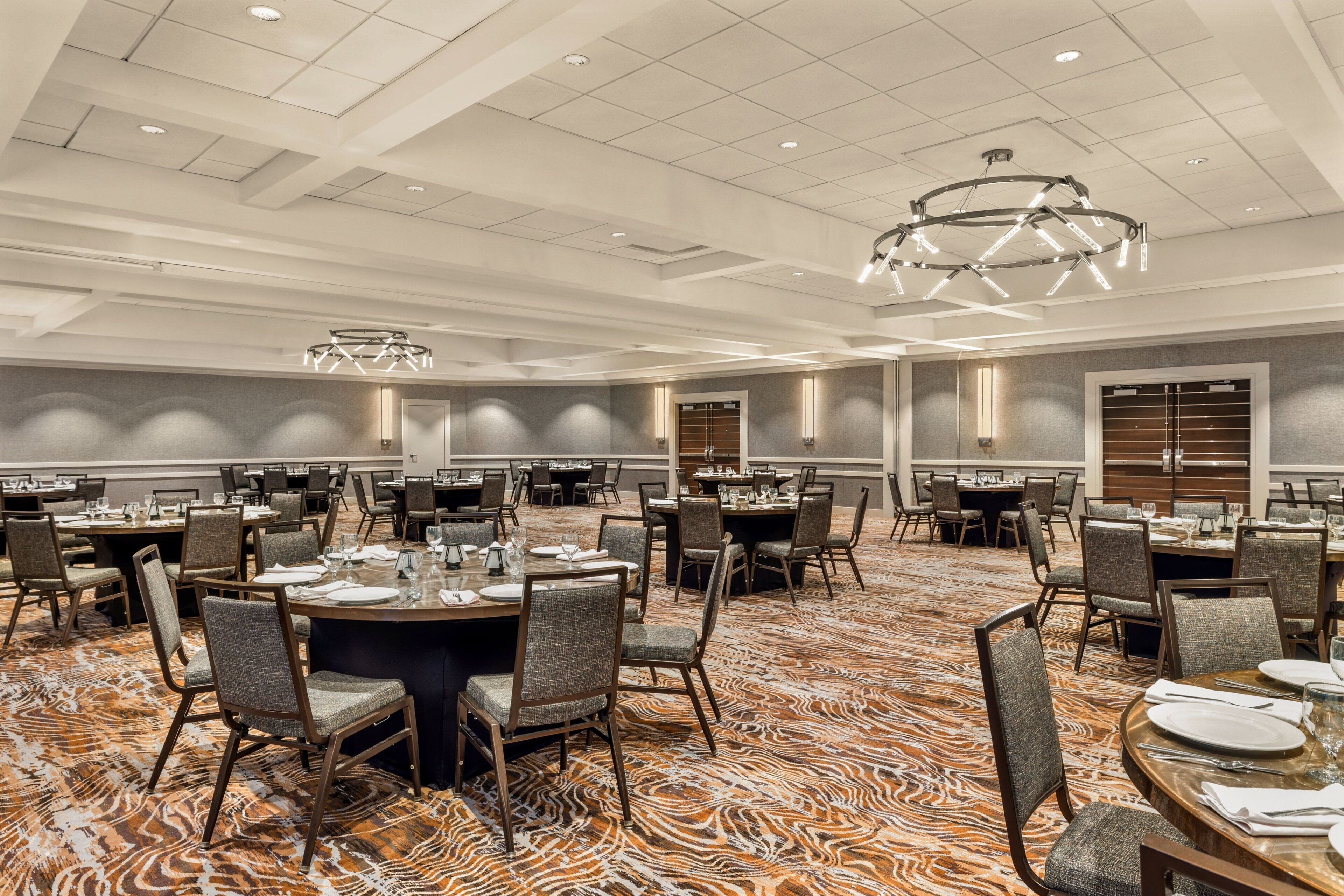 A large banquet hall with round tables, chairs, and a patterned carpet.