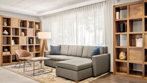 A modern living room with a sectional sofa, a wooden bookshelf, and a small table with a lamp.