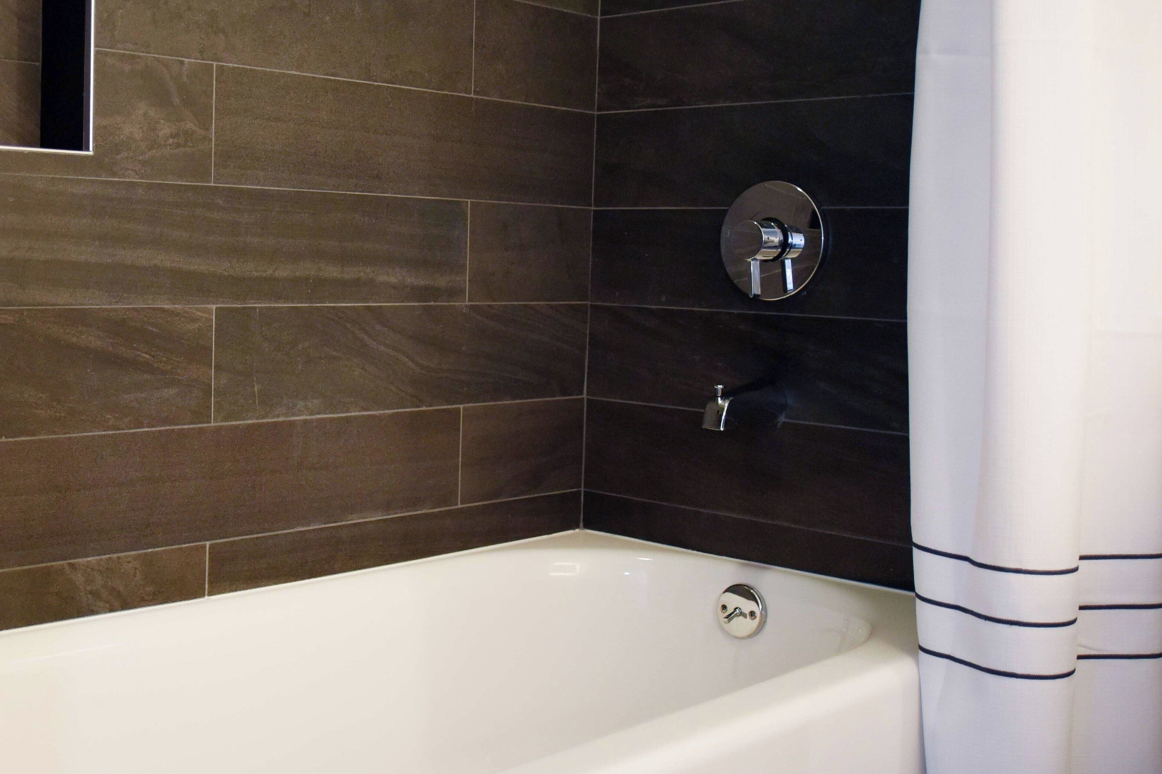 Une salle de bain moderne avec des carreaux brun foncé, une baignoire blanche et un robinet chromé.