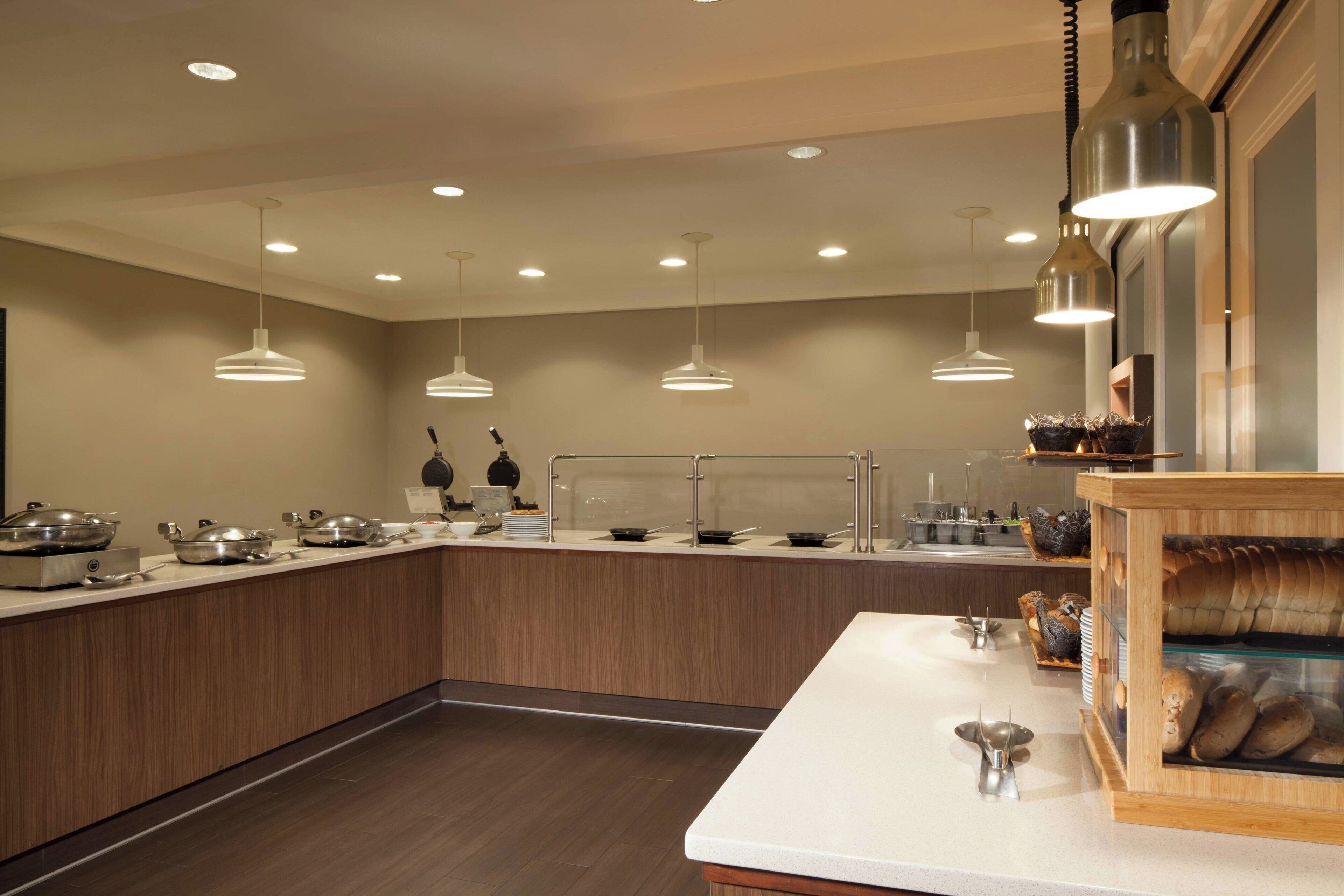 Cuina moderna amb illa central, il·luminació penjant i una vitrina plena de productes de forn.