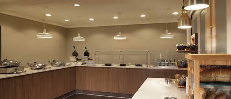 Una cocina moderna con una isla central, iluminación colgante y una vitrina con productos de repostería.