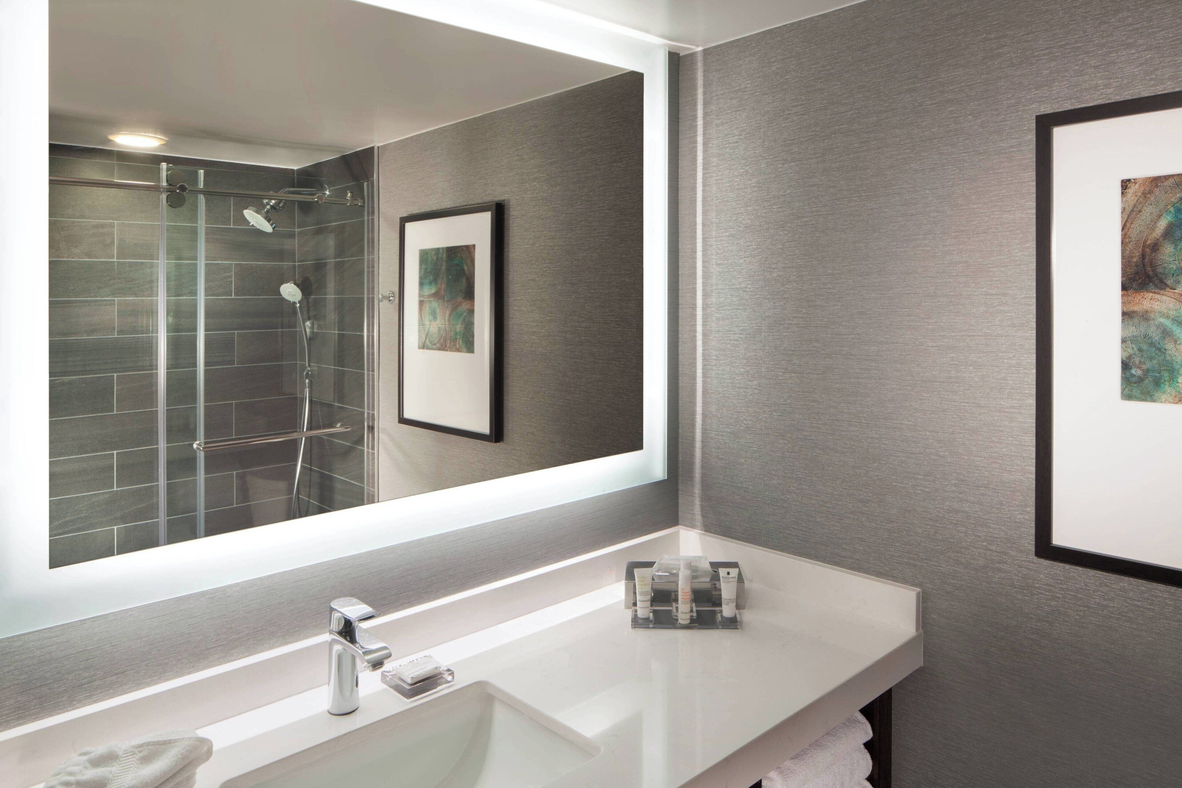 A modern bathroom with a large mirror, a glass shower enclosure, and a white vanity.