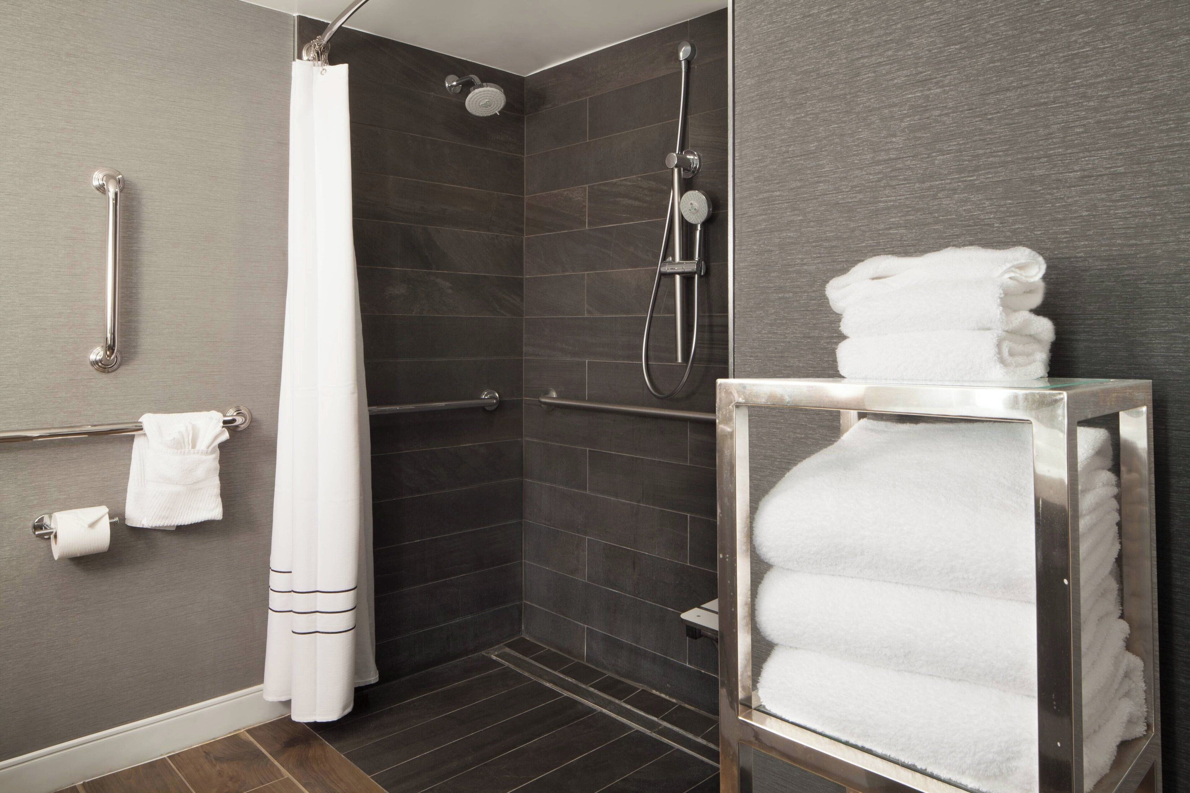 Un baño moderno con ducha, barras de apoyo, toallero y dispensador de toallas de vidrio.