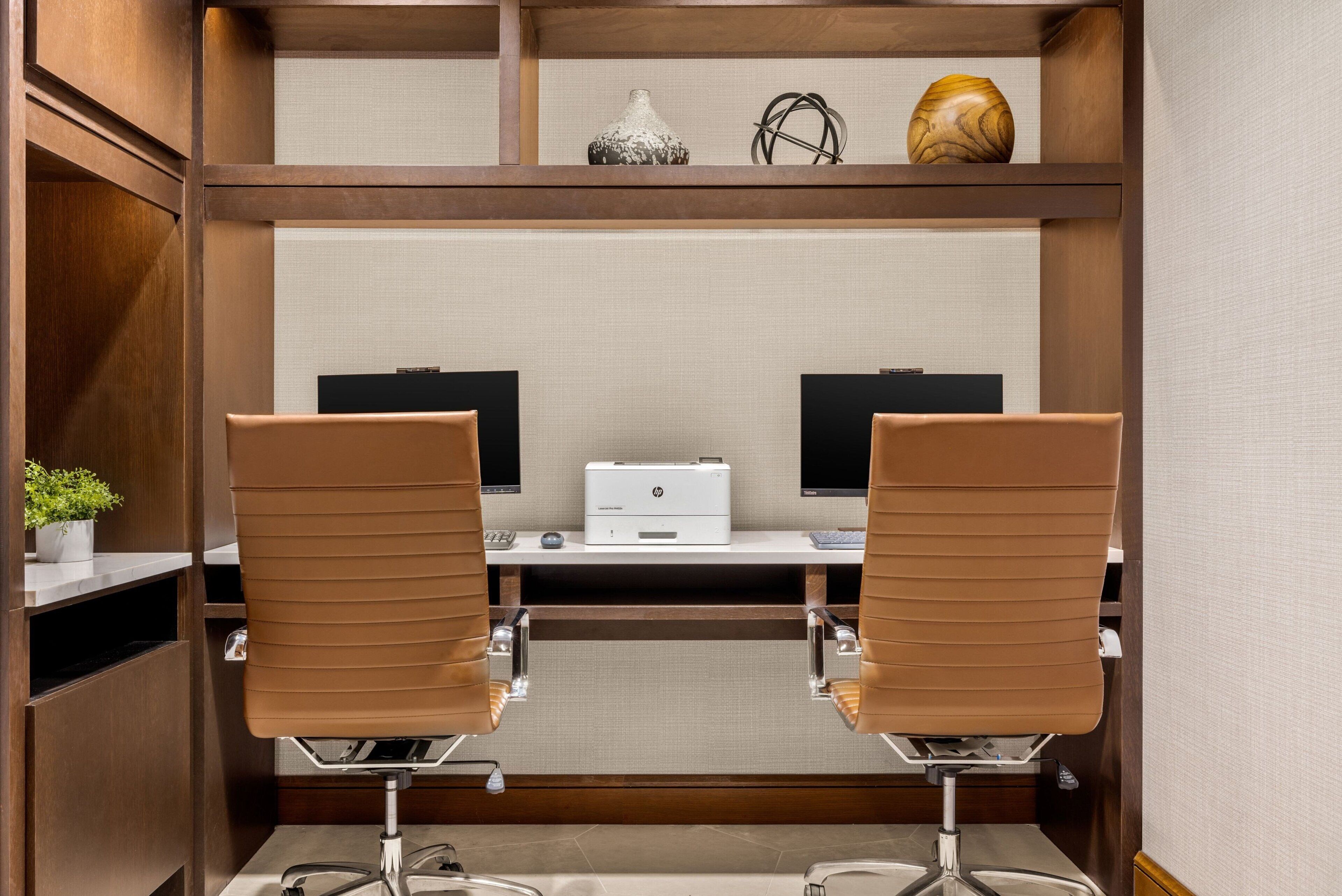 Un espace de bureau moderne comprenant deux chaises marron, un bureau blanc, deux écrans et une imprimante.