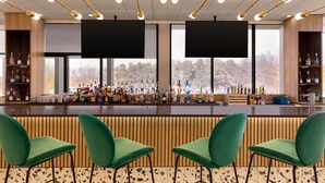 A bar area with green chairs, a wooden bar counter, and shelves of bottles. - Wyndham Garden Atlanta Airport (College Park)