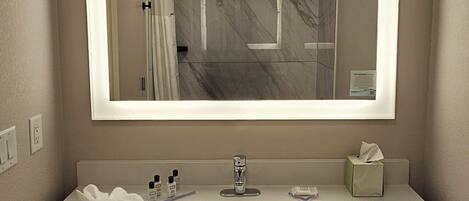 Un baño moderno con un espejo grande, lavamanos blanco y varias toallas.