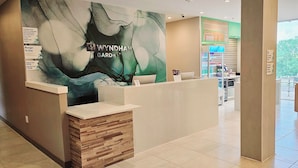 A reception area with a modern design, including a reception desk, a large abstract mural, and a view of the garden. - Wyndham Garden Atlanta Airport (College Park)