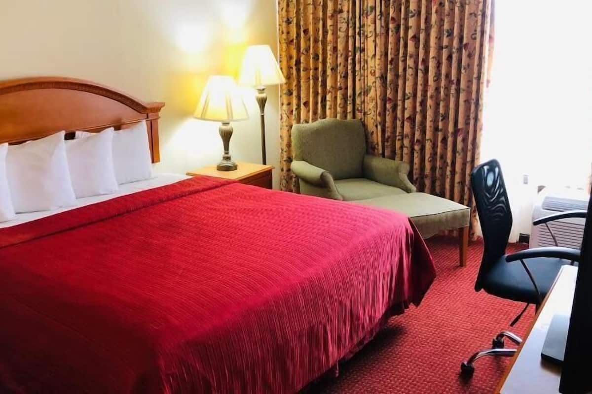 A hotel room with a bed, a chair, a desk, a lamp, and curtains.