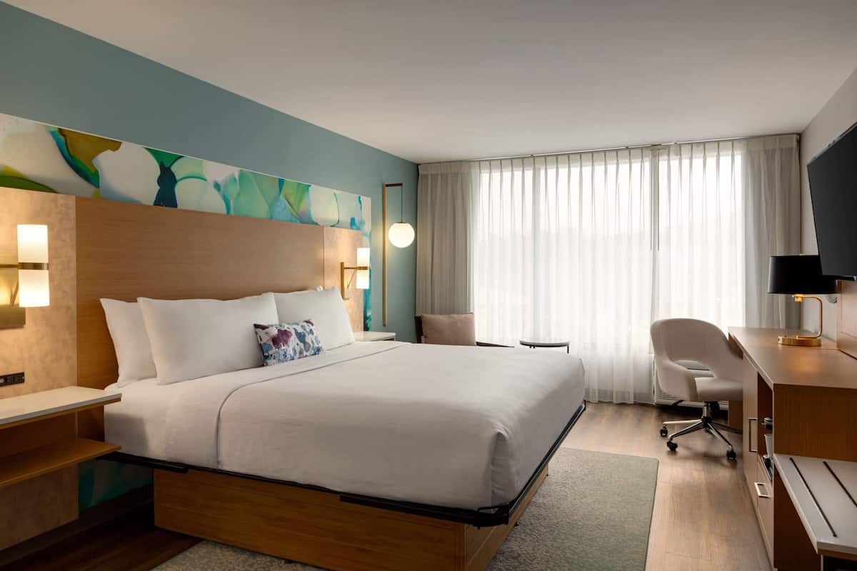 A hotel room with a bed, desk, chair, and a TV.