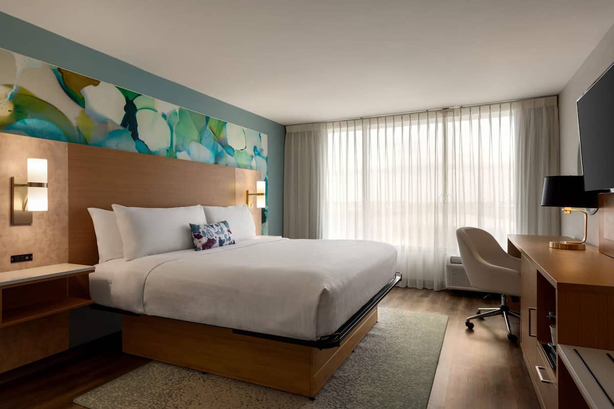 A modern hotel room with a large bed, a desk, and a television.