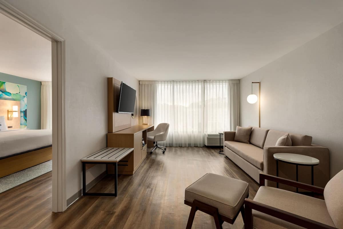 A hotel room with a bed, a desk with a chair, a sofa, a small table, and a TV.