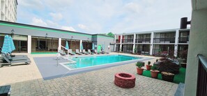 A swimming pool with lounge chairs and umbrellas, surrounded by potted plants and a brick fire pit. - Wyndham Garden Atlanta Airport (College Park)