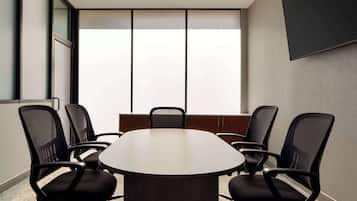 A conference room with a round table, six black chairs, and a large window with blinds.