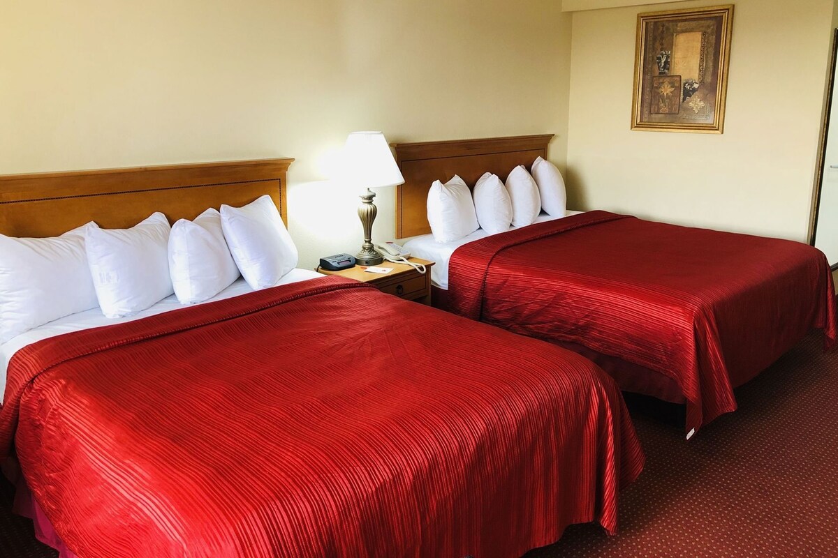 Habitación de hotel con dos camas, una mesita de noche, una lámpara y un cuadro en la pared.