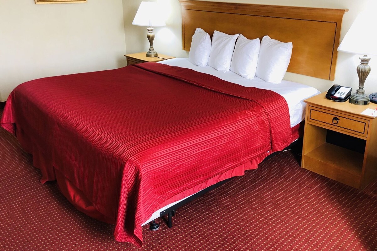Habitación de hotel con una cama grande, cabecera de madera, mesita de noche con lámpara y teléfono.