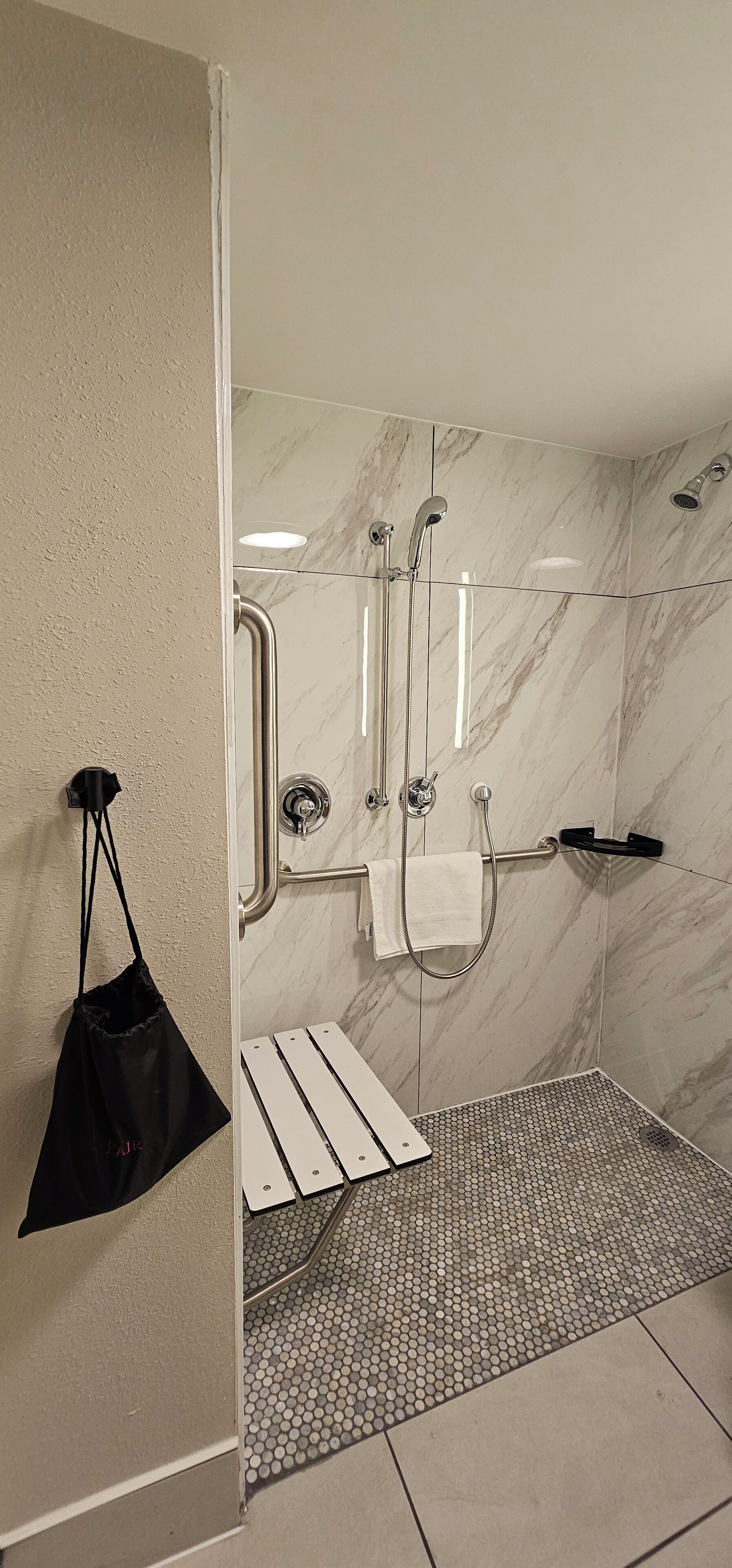 A modern bathroom with a glass shower enclosure, a white towel rack, and a black bag hanging on the wall.