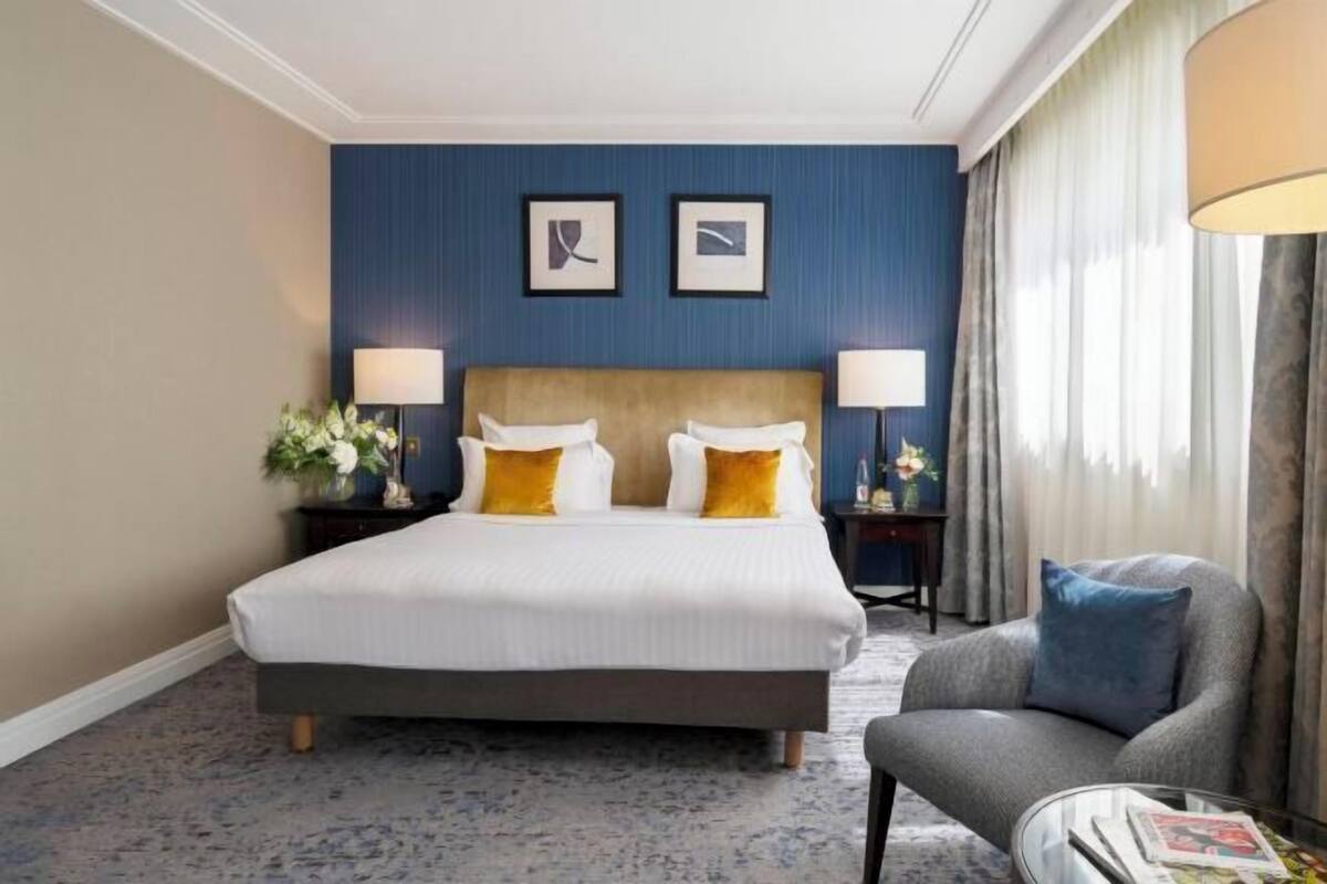 A hotel room with a large bed, two bedside tables with lamps, a chair, and a window with curtains.