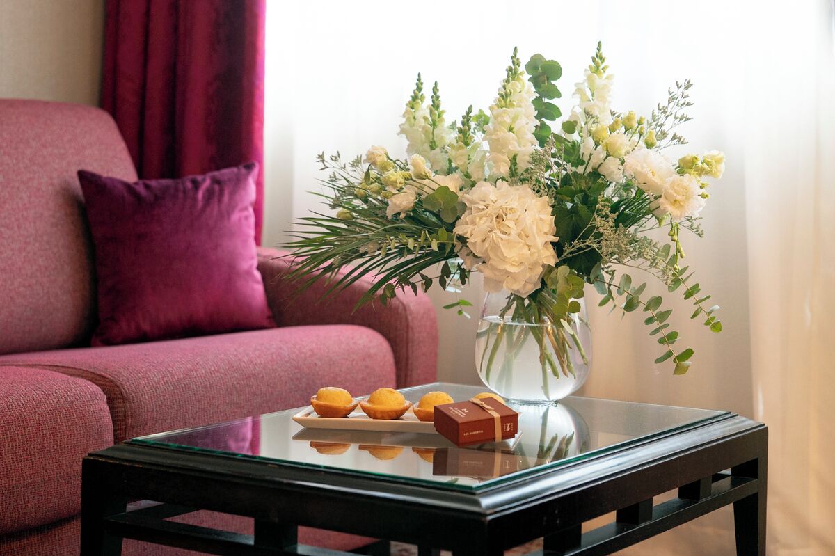 Una sala de estar con un sofá, una mesa de centro de vidrio con un florero y una caja de bombones.