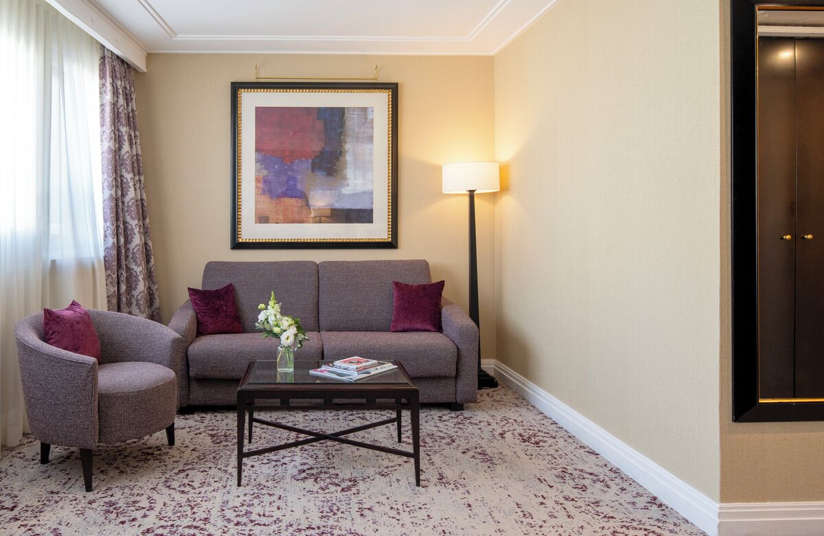 A living room with a sofa, armchair, coffee table, and a framed abstract painting.