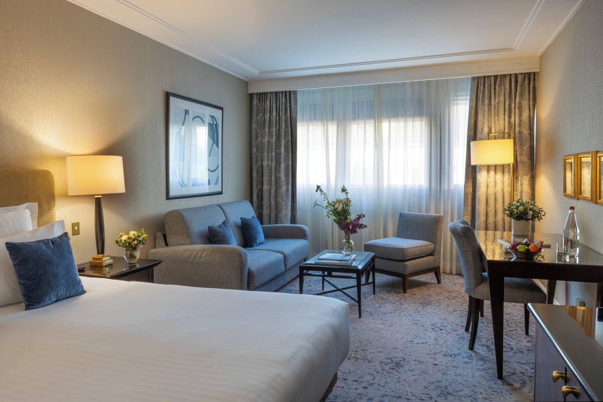 A hotel room with a bed, two sofas, a coffee table, a desk, and a chair.