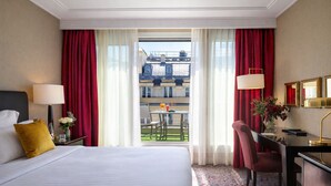 Habitación de hotel con cama, escritorio, silla, lámpara y vista al balcón exterior.