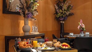 Una mesa de desayuno con diversos alimentos, un jarrón con flores y un espejo en la pared.
