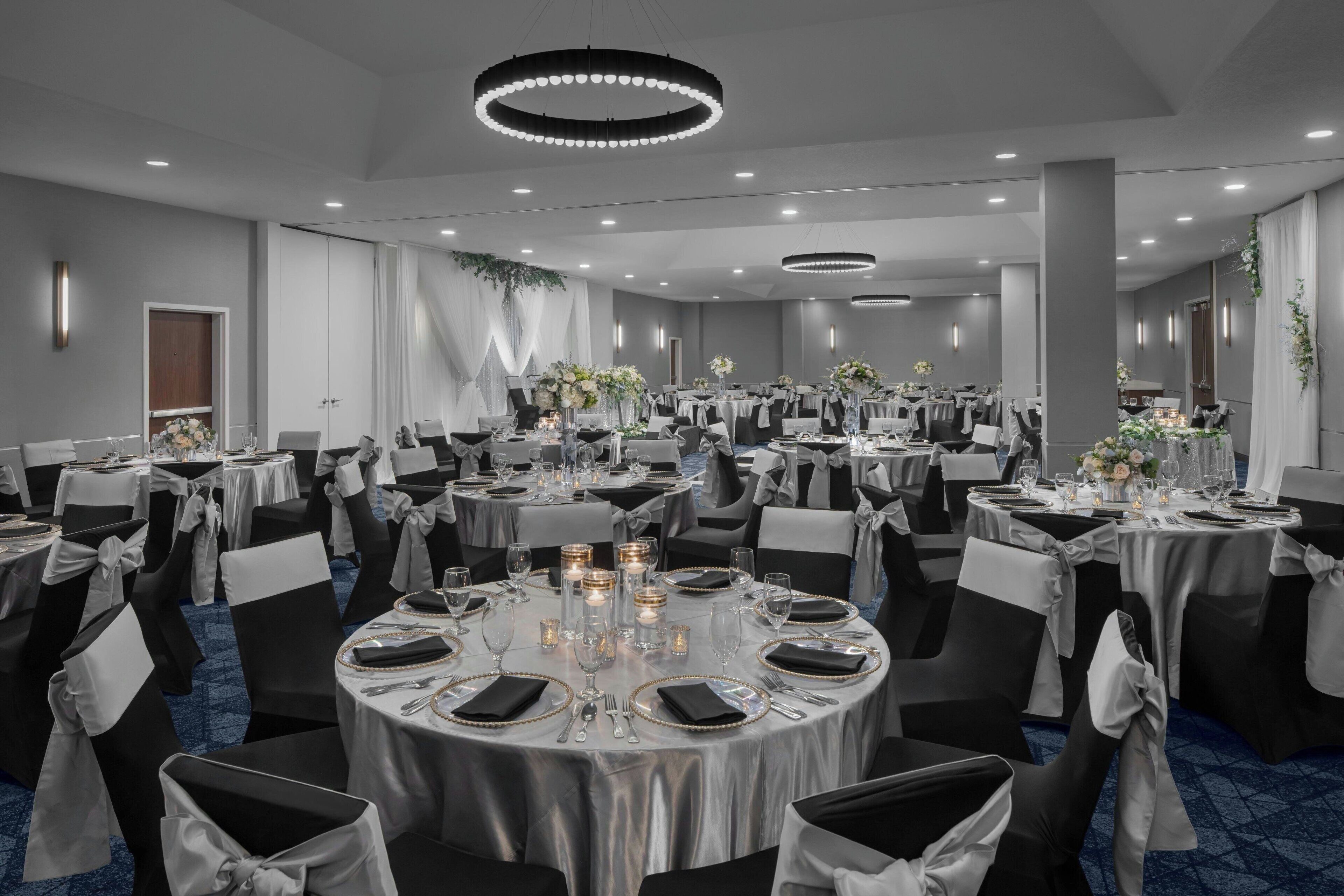 A banquet hall with round tables, black and white chairs, and chandeliers.
