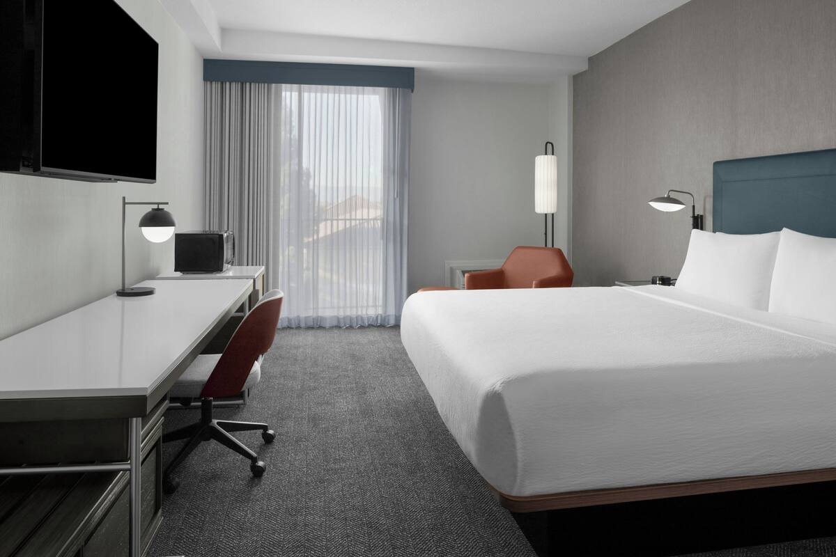 A hotel room with a bed, desk, chair, and a TV.