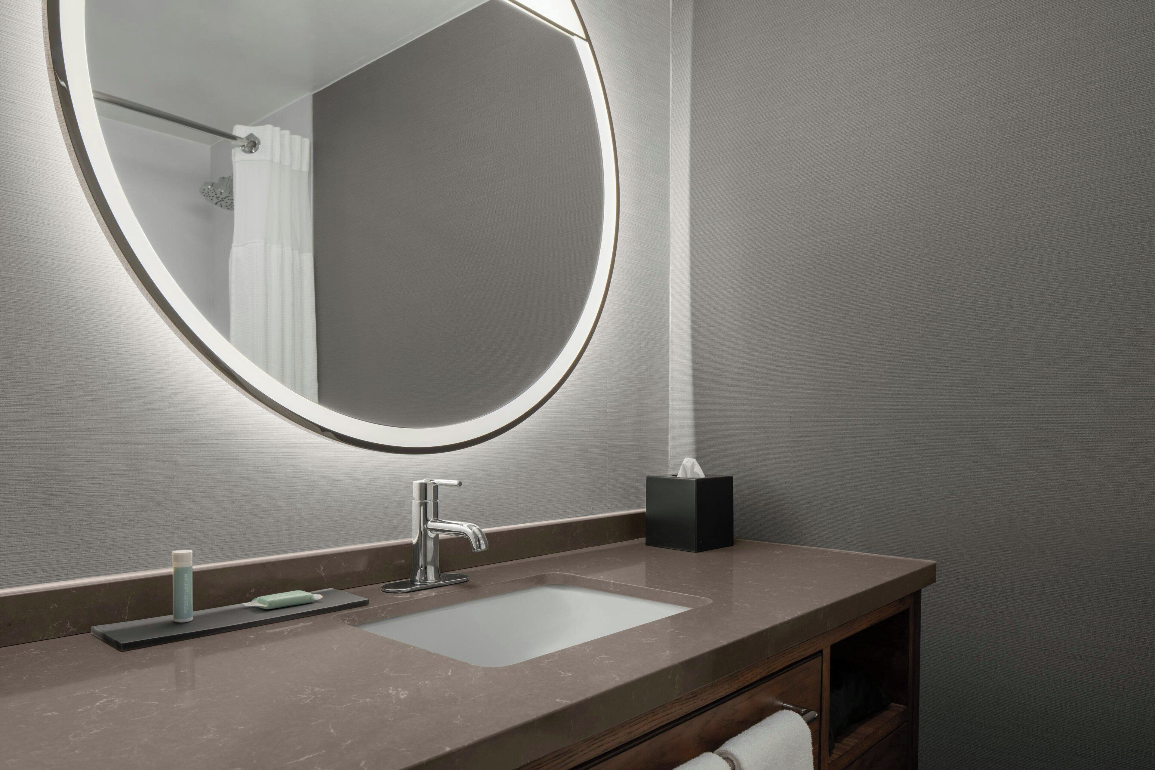 Een badkamer met een ronde spiegel, een wastafel en een handdoekhouder.
