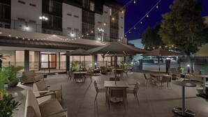 An outdoor patio area with tables and chairs, string lights, and umbrellas.
