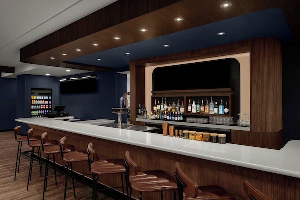 A bar area with a long counter, multiple stools, and a well-stocked bar with various bottles.