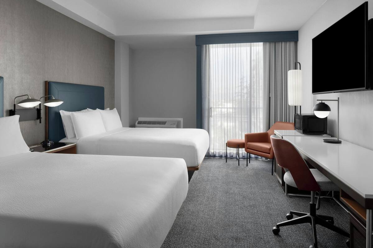 A hotel room with two beds, a desk, a chair, a TV, and a window with curtains.