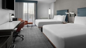 A hotel room with two beds, a desk, a chair, a TV, and a window with curtains.