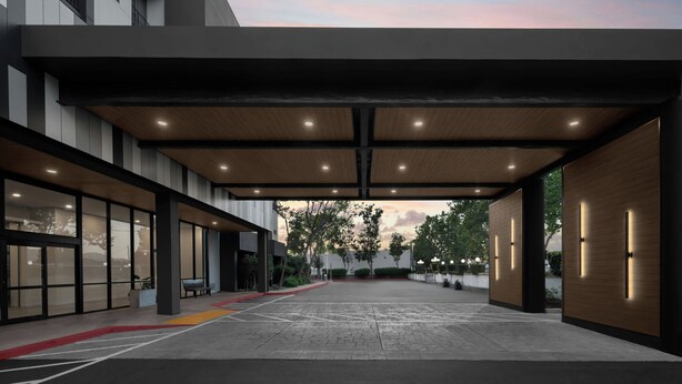 A modern building with a covered entrance, large windows, and a paved area with marked parking spaces.