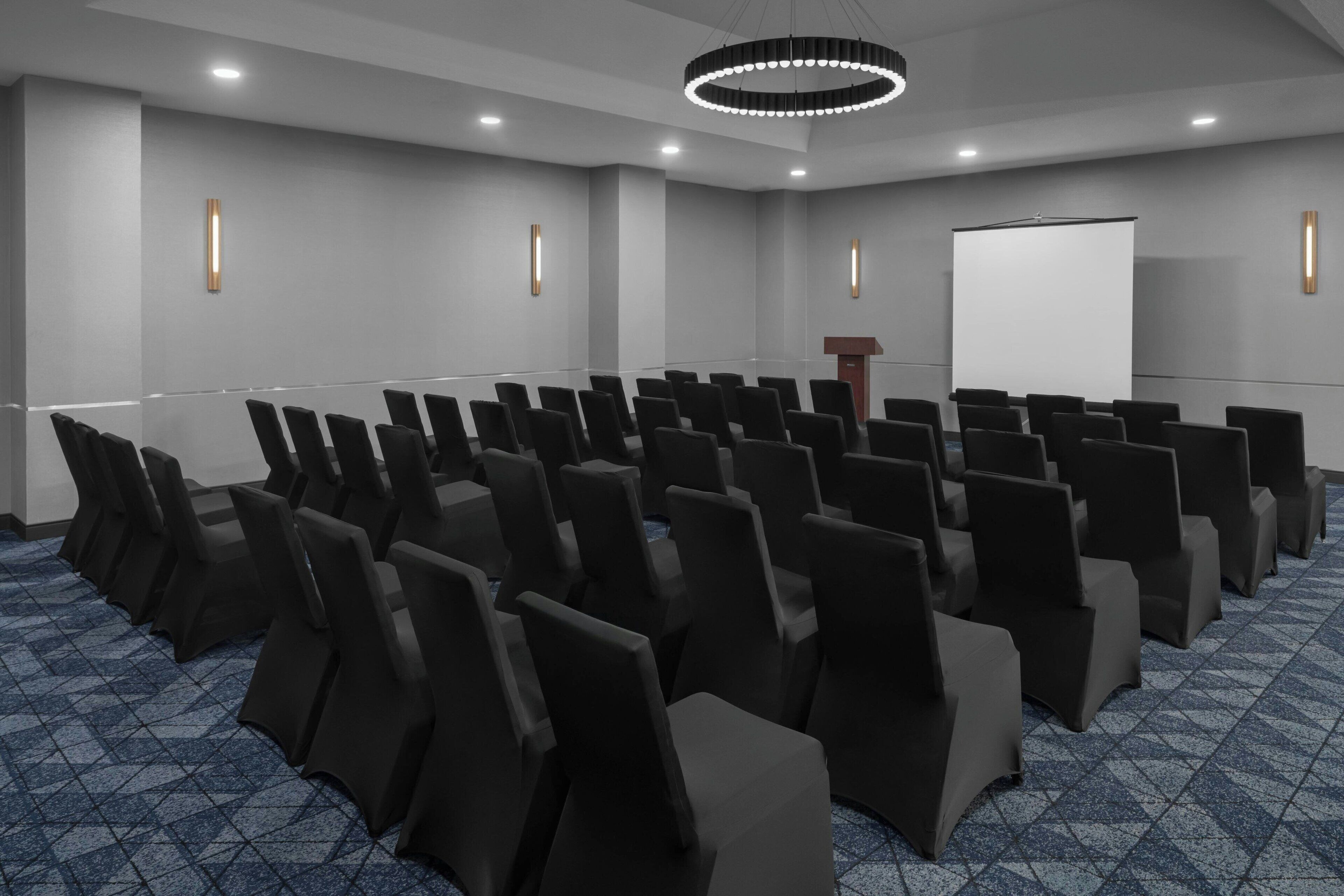 A conference room with rows of chairs, a podium, and a projection screen.