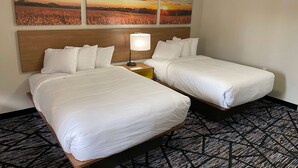 A hotel room with two beds, a nightstand with a lamp, and a large wall painting of a sunset over a field. - Days Inn by Wyndham Lake Charles (Lake Charles)