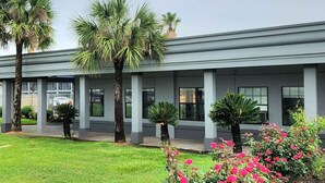 A modern building with a flat roof, large windows, and a well-maintained lawn with palm trees and flowering plants. - Days Inn by Wyndham Lake Charles (Lake Charles)