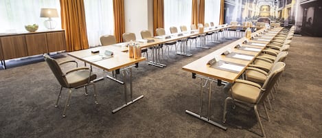 A conference room with long tables and chairs, a carpeted floor, and large windows with curtains.