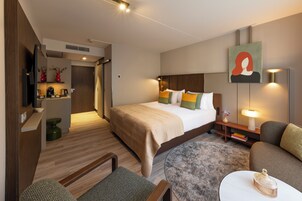 Una habitación de hotel moderna con una cama grande, un sofá, una mesita y un televisor.