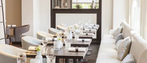 Ein Restaurant mit einem langen Esstisch, bequemen Sitzgelegenheiten und hängenden Pendelleuchten.