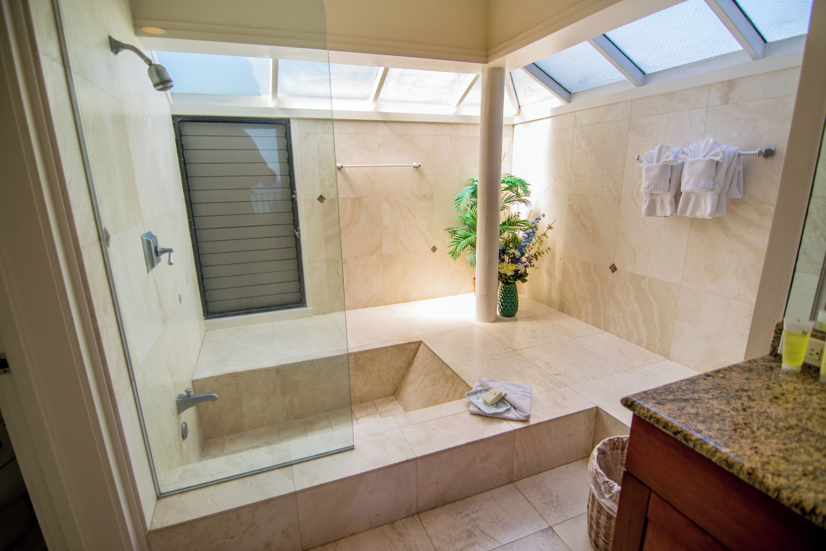 A modern bathroom with a glass-enclosed shower, a built-in bench, and a large window providing natural light.
