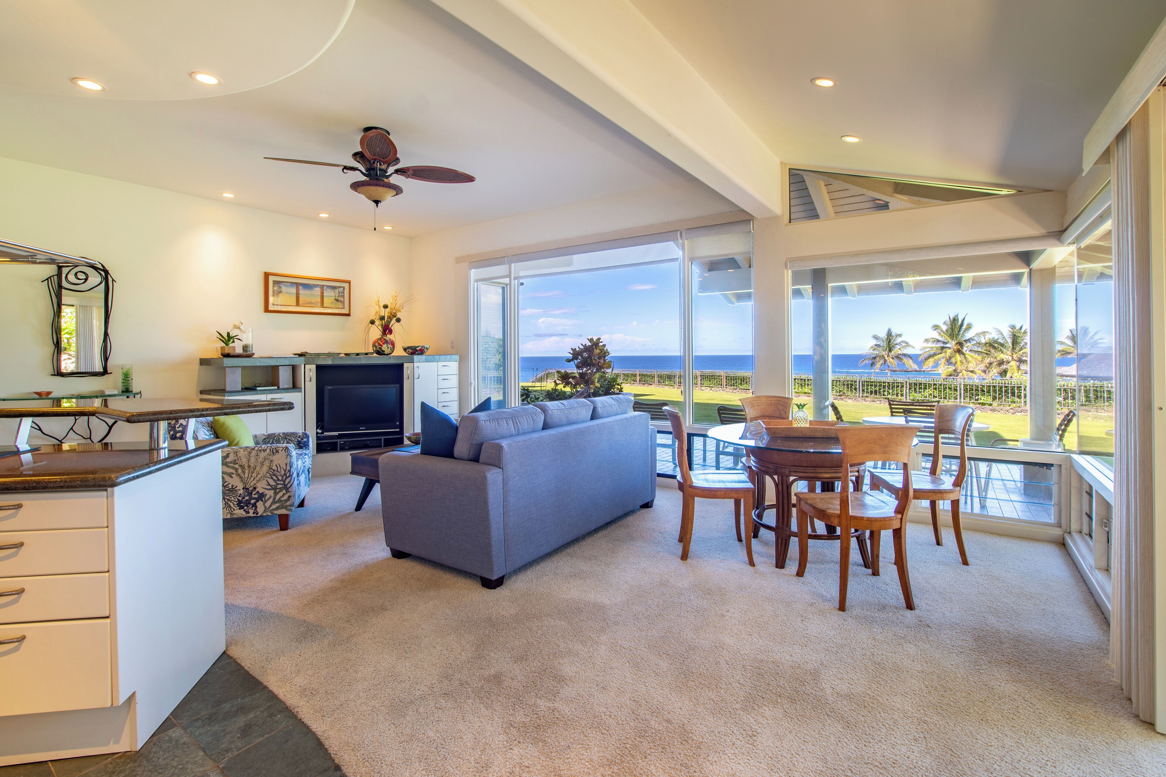 Un'ampia zona giorno con una grande finestra vista panoramica, una sala da pranzo con sedie in legno e una ventola a soffitto.