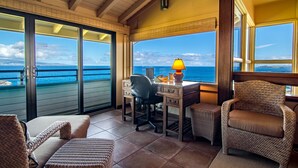 A balcony with a desk, chairs, and a view of the ocean.