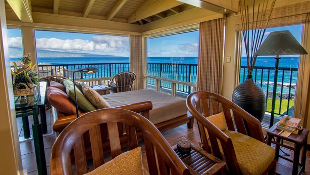 A balcony with wooden furniture, a large vase, and a view of the ocean.
