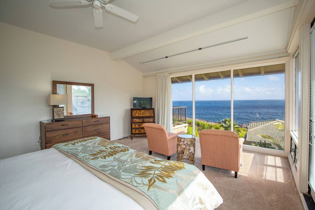 Ein Schlafzimmer mit Bett, Schminktisch, Fernseher und einem Balkon mit Meerblick.