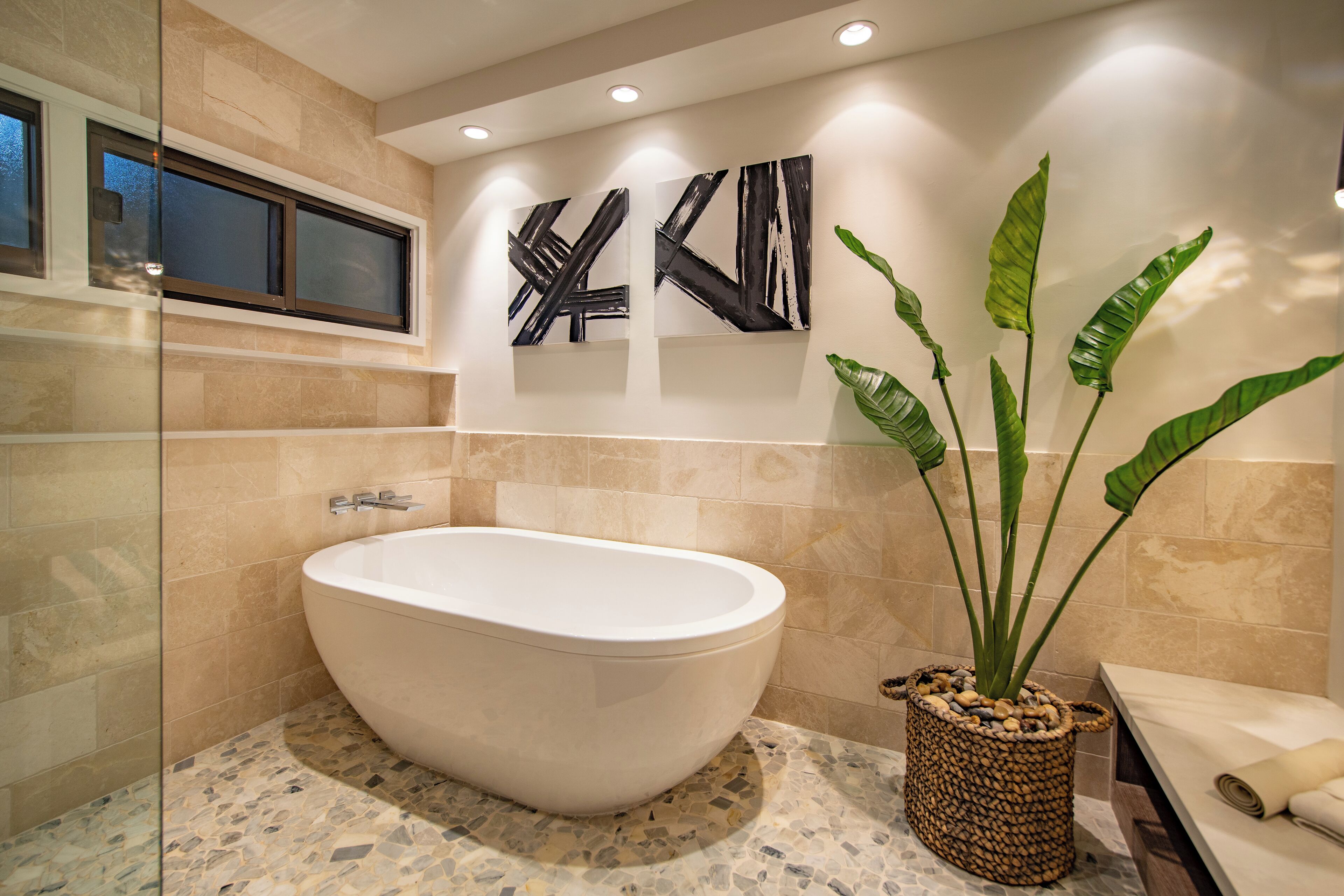 A modern bathroom with a freestanding bathtub, a large potted plant, and abstract wall art.
