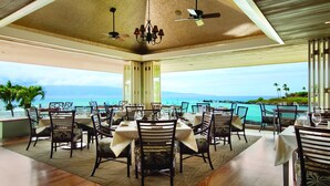 A restaurant with tables and chairs arranged for dining, overlooking a scenic ocean view.