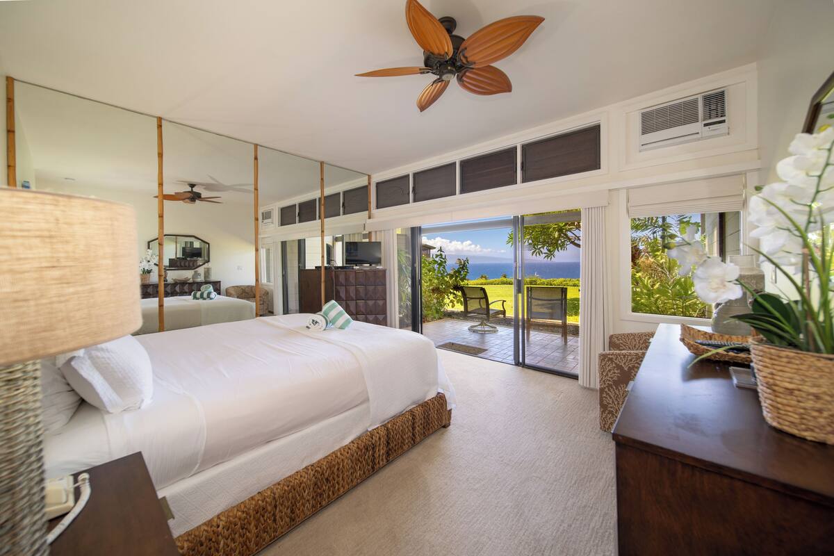 Ein Schlafzimmer mit einem großen Bett, einem Deckenventilator, einem Fernseher und Meerblick durch eine Schiebetür.
