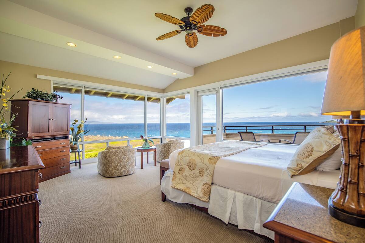 Ein Schlafzimmer mit einem großen Bett, einem Deckenventilator, einem Schreibtisch und Blick auf den Ozean.